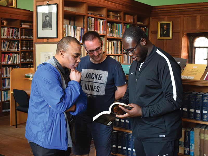 Three men in a library looking at a book